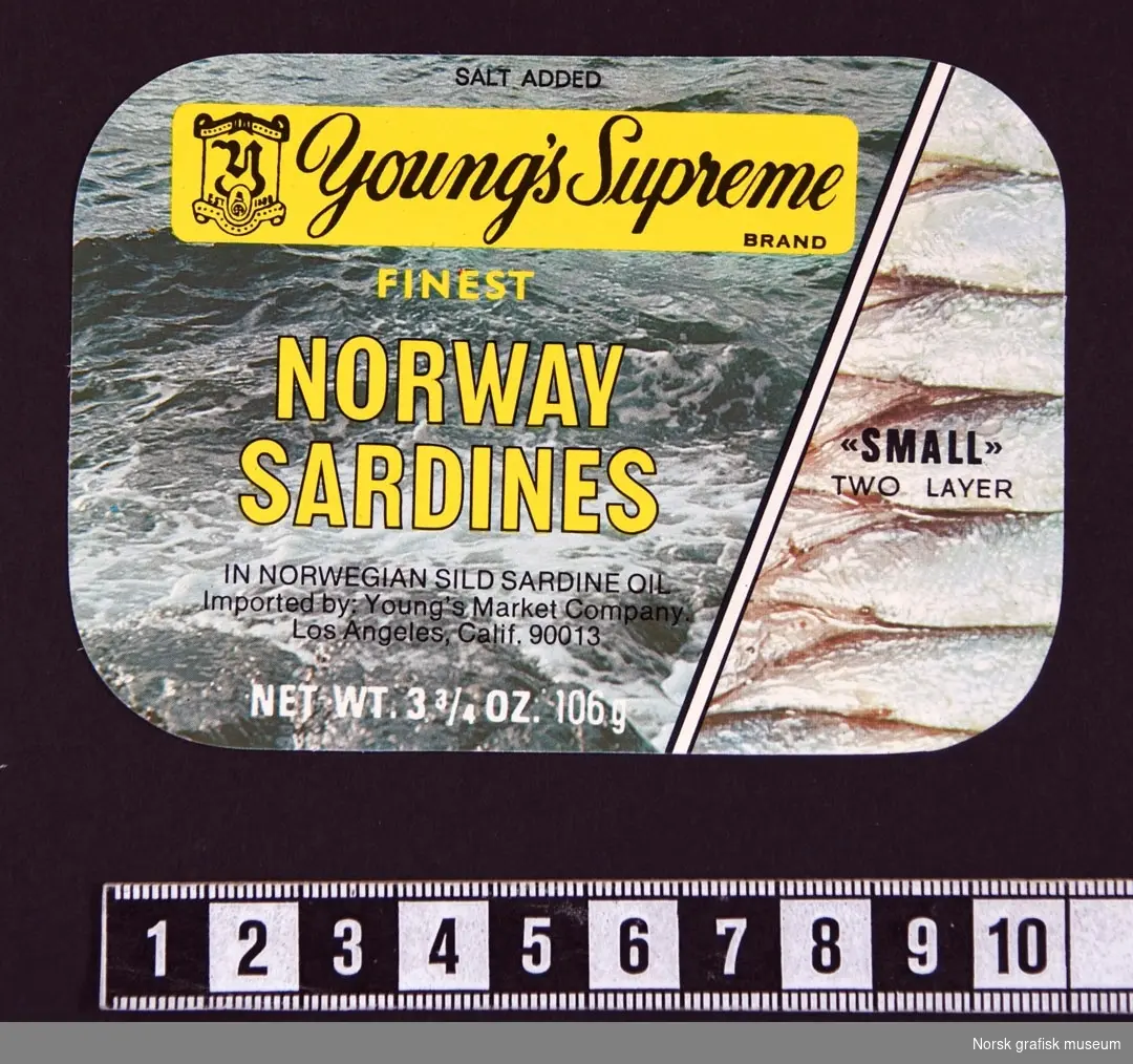Etikett med en bakgrunn delt diagonalt og som viser foto av sjø eller vann på venstr side, og i boksen på høyre side. Over bakgrunnen står varebeskrivelsen i gult og sort. 

"Finest Norway sardines in Norwegian sild sardine oil"