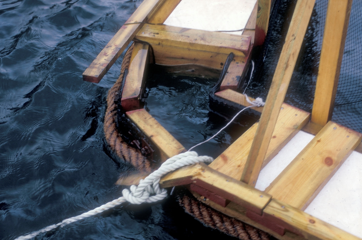 Detaljbilde av ei merde. Bildet viser hvordan hjørnene ble forsterket med bildekk for ikke å brekke i stykker ved sjøgang. Bildet er tatt i forbindelse med Lovund seminaret i 1972.