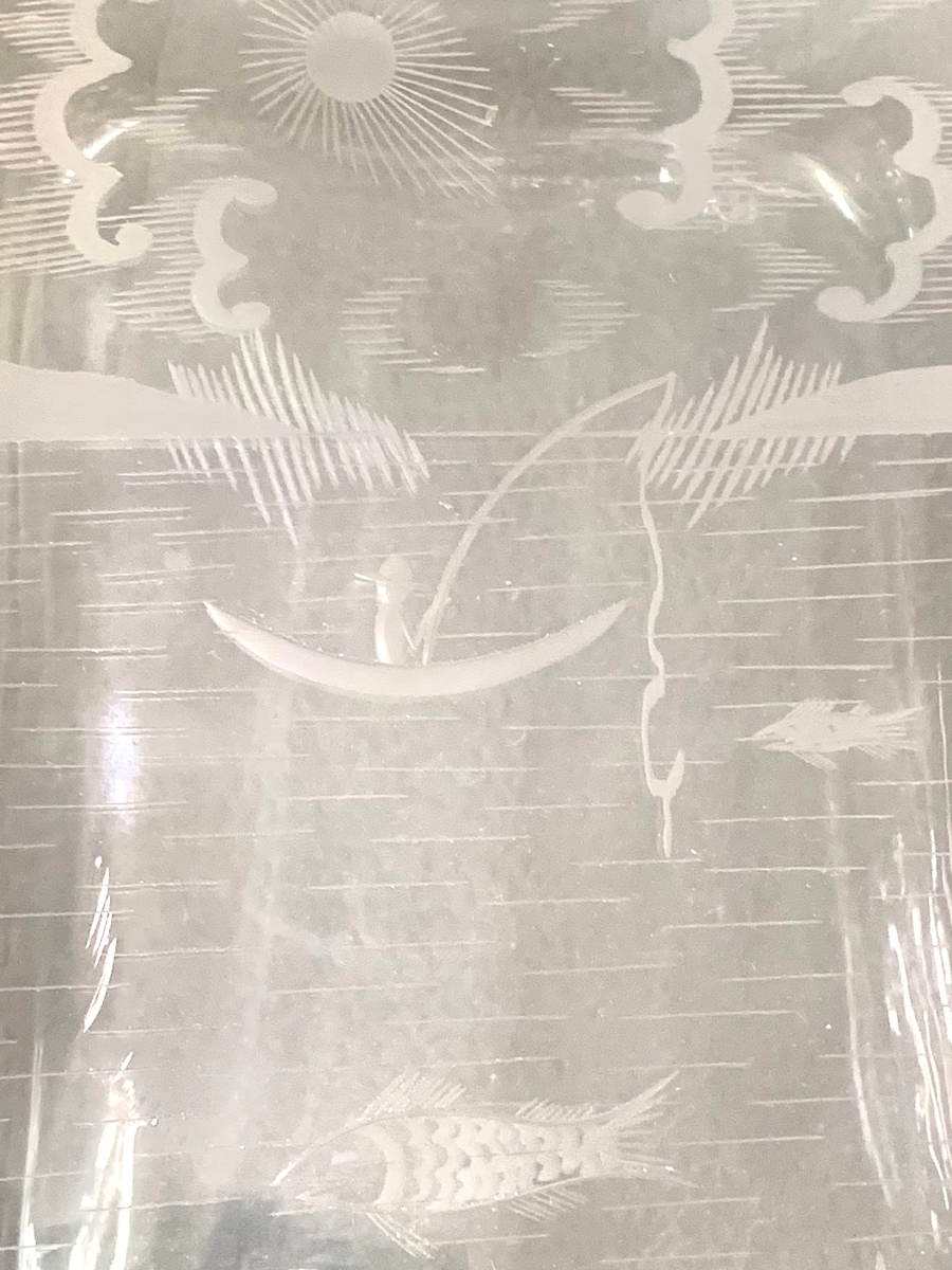 Fyrkantig brännvinsflaska med graverad dekor i form av en metande man på en sjö. I vattnet syns fiskar.
Etikett: Brun botten med svart text "J G"