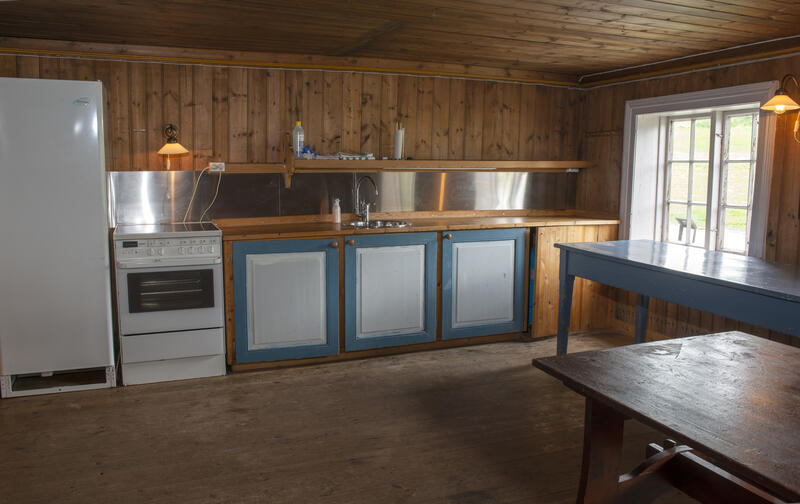 Løtenbygningen har et romslig kjøkken med umalte vegger av laftet tømmer og panel, blåmalt kjøkkeninnredning og hvitevarer.