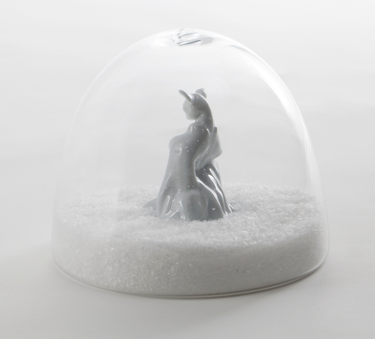 Hvit porselensfigur med rådyrhode og menneskekropp, plassert i omsluttende glasskuppel med kunstige snøfnugg.