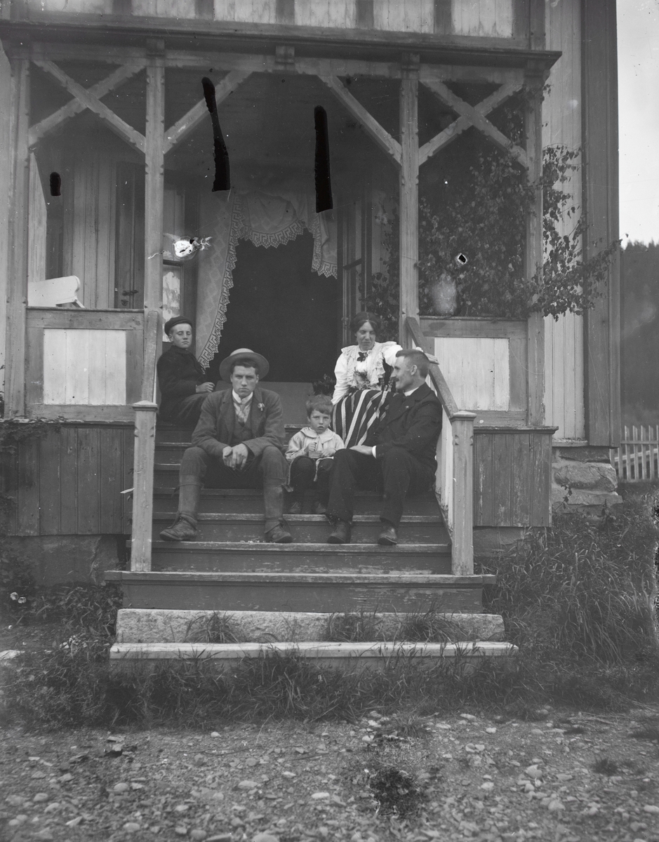 Gruppeportrett av familien Aston som sitter i trappa til et bolighus.