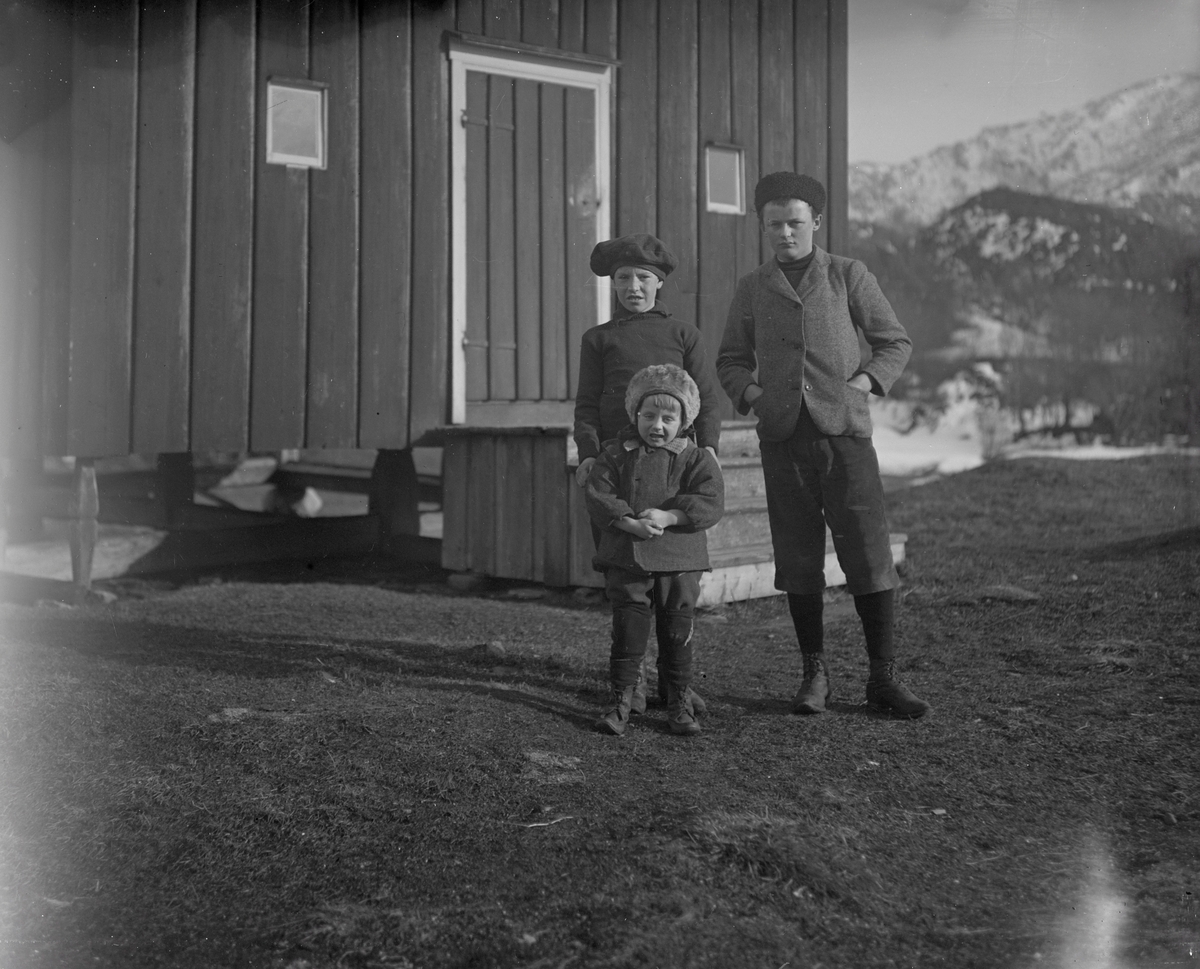 Gruppeportrett av tre barn av familien Aston foran et hus. Finnmark?