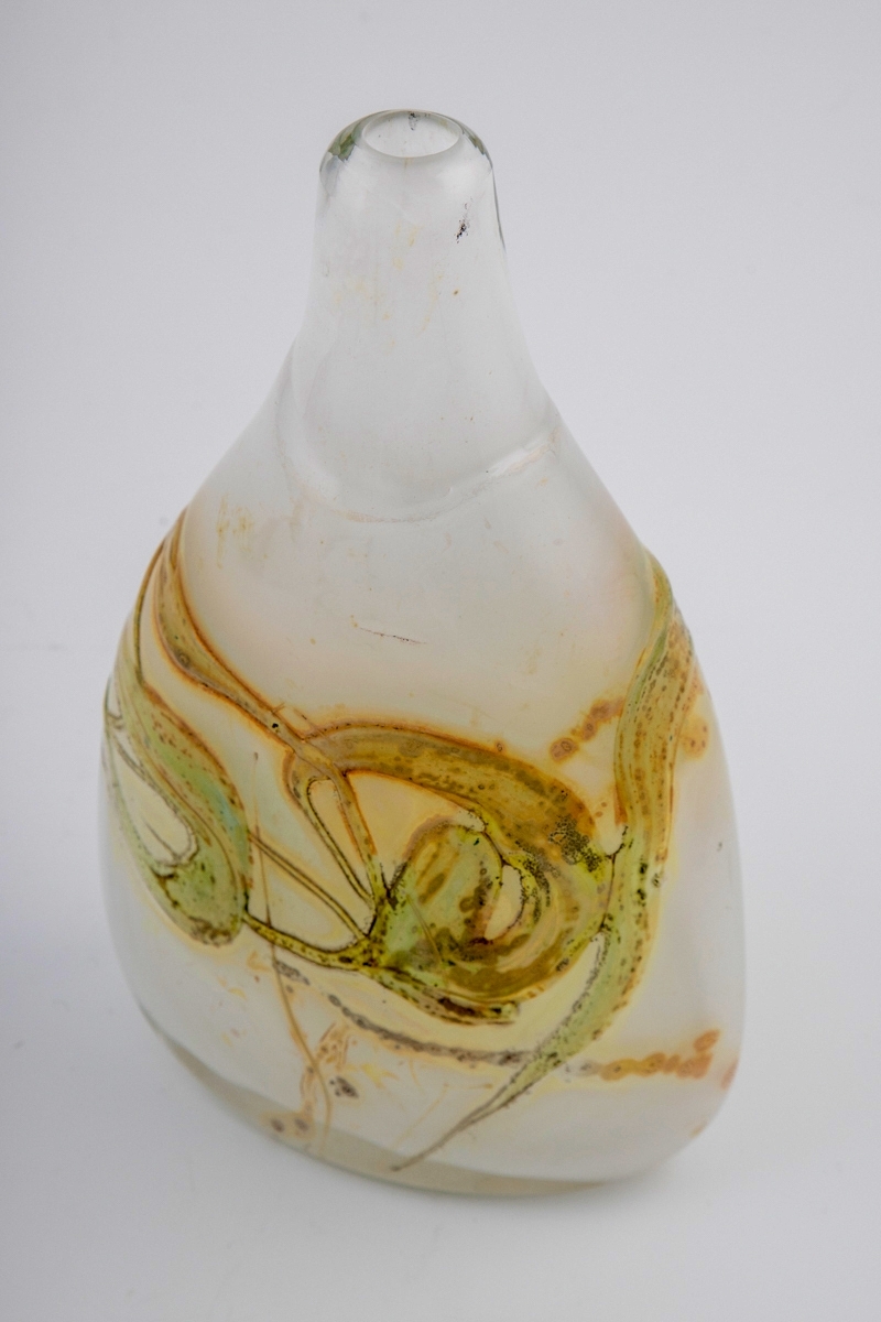 Flattrykket dråpeformet vase med lav hals. Vasen er utført i opakt melkehvitt glass i underfangsteknikk, med irisert overflate. Korpus er dekorert med slyngende gulgrønne partier, og hviler på en oval fotring.