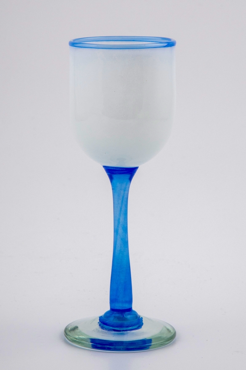 Vinglass med hvit halvgjennomskinnelig kupa. Munningen er markert med en blålig rand. Stetten er utført i klart blåfarget glass, og hviler på en sirkulær fot med puntemerke.