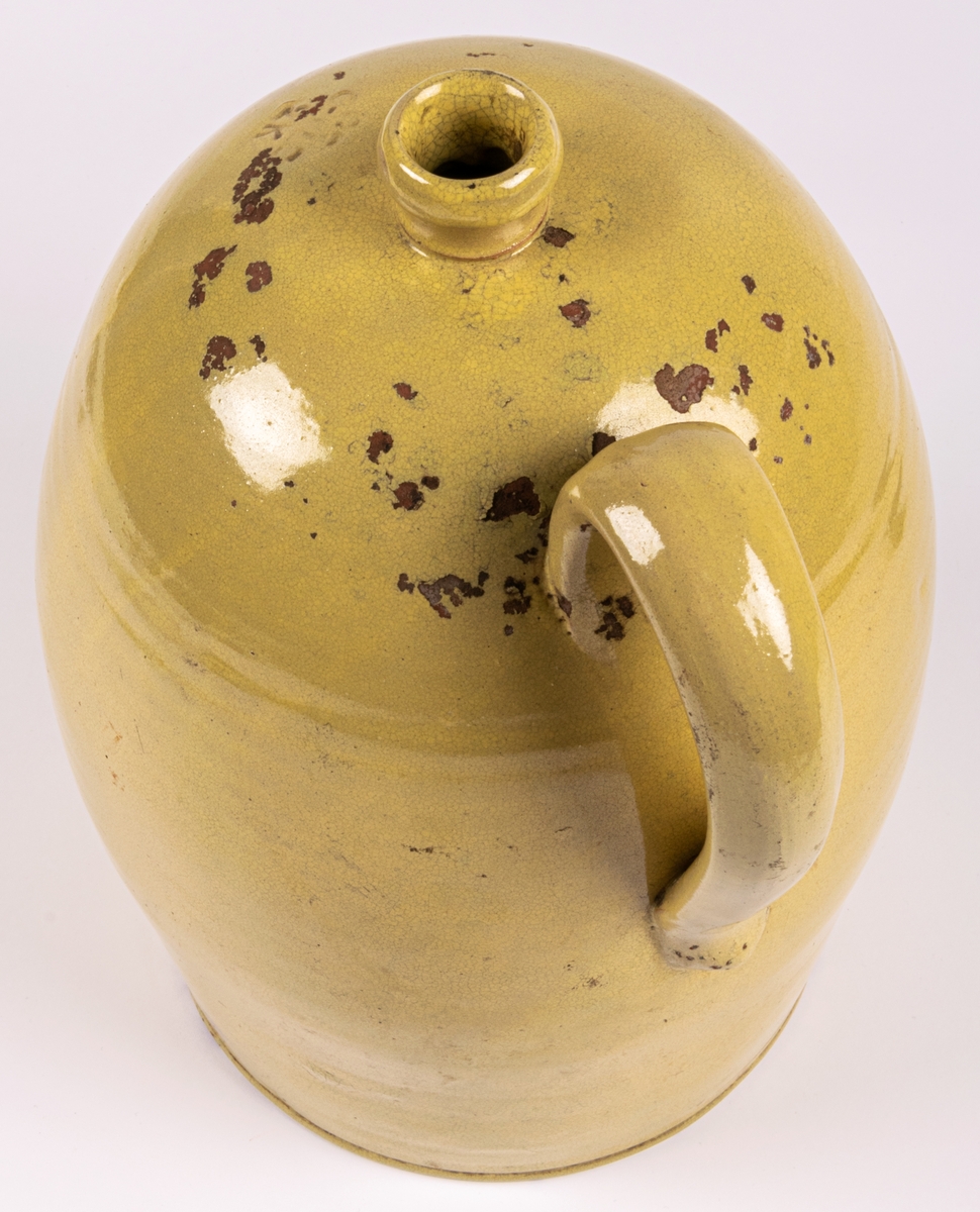 Brännvinskrus, gulglaserat lergods, drejat med en hänkel. Tillverkat vid Bo Fajans, stämplat på undersidan B GEFLE 2 K.