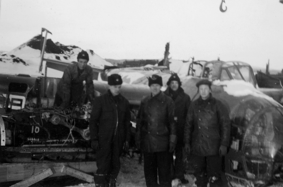 Flygvapenpersonal samlade vid bärgat flygplan B 18 på kajen i Härnösands hamn efter nödlandning på isen den 10 februari 1946. Motorerna har demonterats. Vy framifrån.