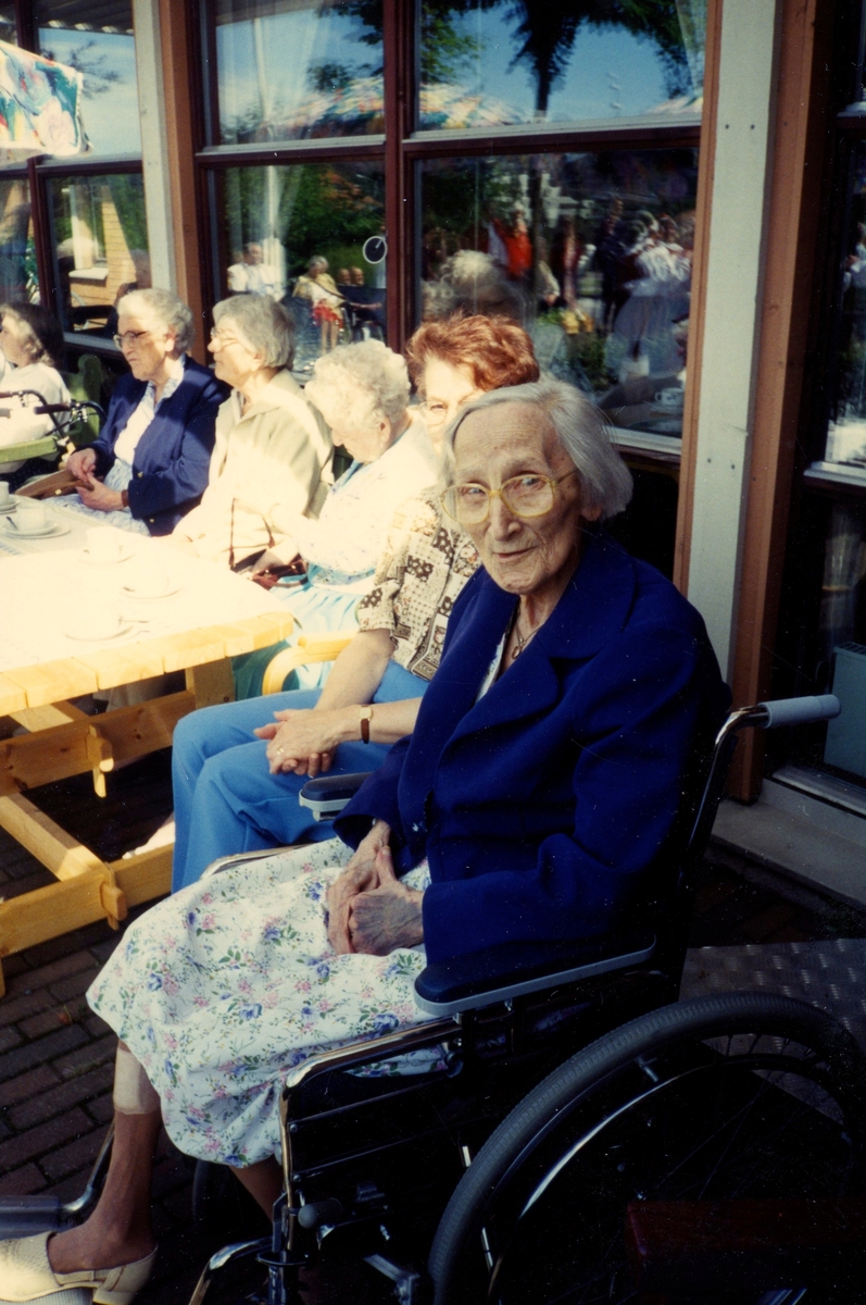 Fem kvinnor sitter och njuter av solen utanför Brattåsgården (Streteredsvägen 5), cirka 1990. Från vänster: (i glasögon, mörk jacka) Rut Göransson (1905 - 1999), Edit Bernhardsson (1911 - 2000), Maria Valvsten (1909 - 2004), vårdbiträde Agneta samt Sigrid Börjesson (1910 - 1995).