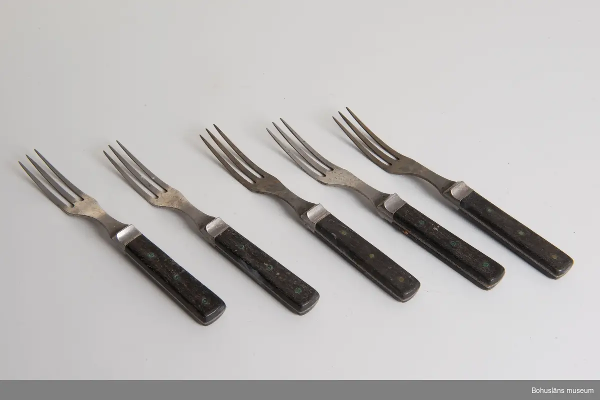 Trekloig gaffel med svart träskaft. Mellan skaft och gaffel metallskoning som buktar ut. Snarlik med UM17095 och med UM17097.
