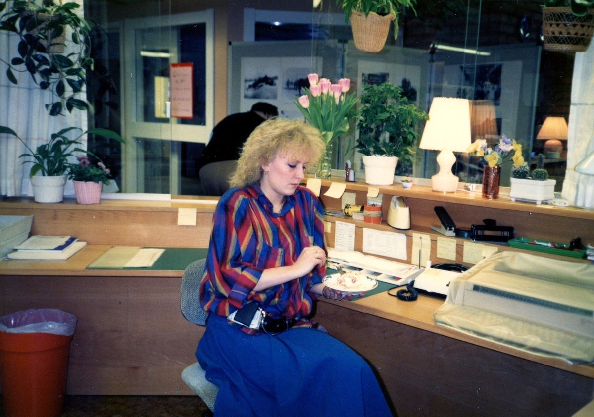 Ett kvinnligt vårdbiträde äter en bakelse i Brattåsgårdens reception, cirka 1986 - 1990.