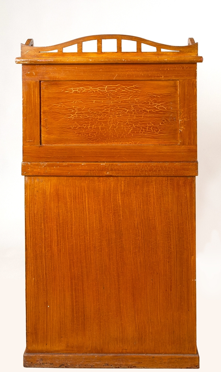 Pulpet, butiksinredning, av trä med brun ådermålning. På några ställen syns röd färg under den bruna. Möbeln består av två delar. Överdelen har lutande skrivplan krönt med ett lågt, böljande galler längs den bakre långsidan (mot kunden). Under skrivskivan finns två draglådor försedda med plasthandtag och nyckelhål med lås. Den övre lådan är tom. Den undre lådan innehåller en kassalåda med tre fack för mynt och sedlar. Kassalådan är försedd med nyckelhål och lås. I kassalådan fanns vid förvärvstillfället en nyckel, ett 1-öres kopparmynt från 1940 och en mindre pendel. I den undre lådan fanns också vid förvärvstillfället två rullar med pappersband med tryckt text:"Köp Ur- & Glasögon hos JOH. ENGSTRÖMS Eftr. V. Storgatan 4, jönköping. Telelefon 155". Pulpetens udderdel har en mellanhylla och ett bottenplan.