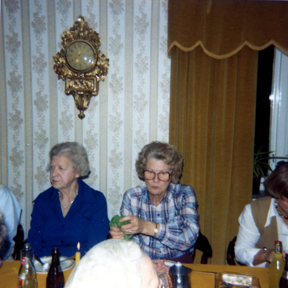 Räkfest för boende och anhöriga i Brattåshemmets matsal (Brattåsvägen 6) 1980-10-16. Tre kvinnor sitter till bords. I bakgrunden hänger en väggpendyl.