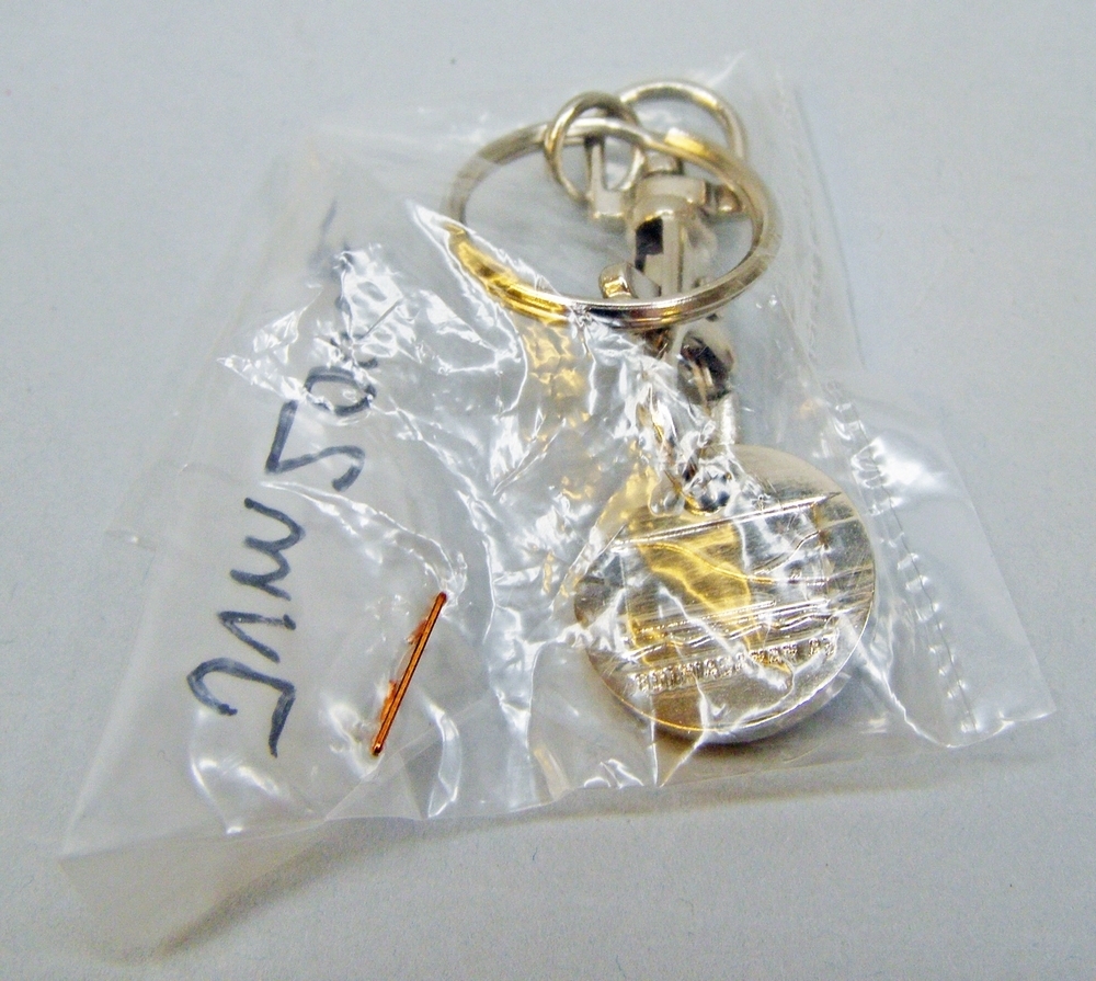 Nyckelring med Botniabanan AB:s logotyp på en attrapp för tio-krona (att sätta i tex kundvagnar). Ringen ligger originalförpackad i en liten plastpåse.