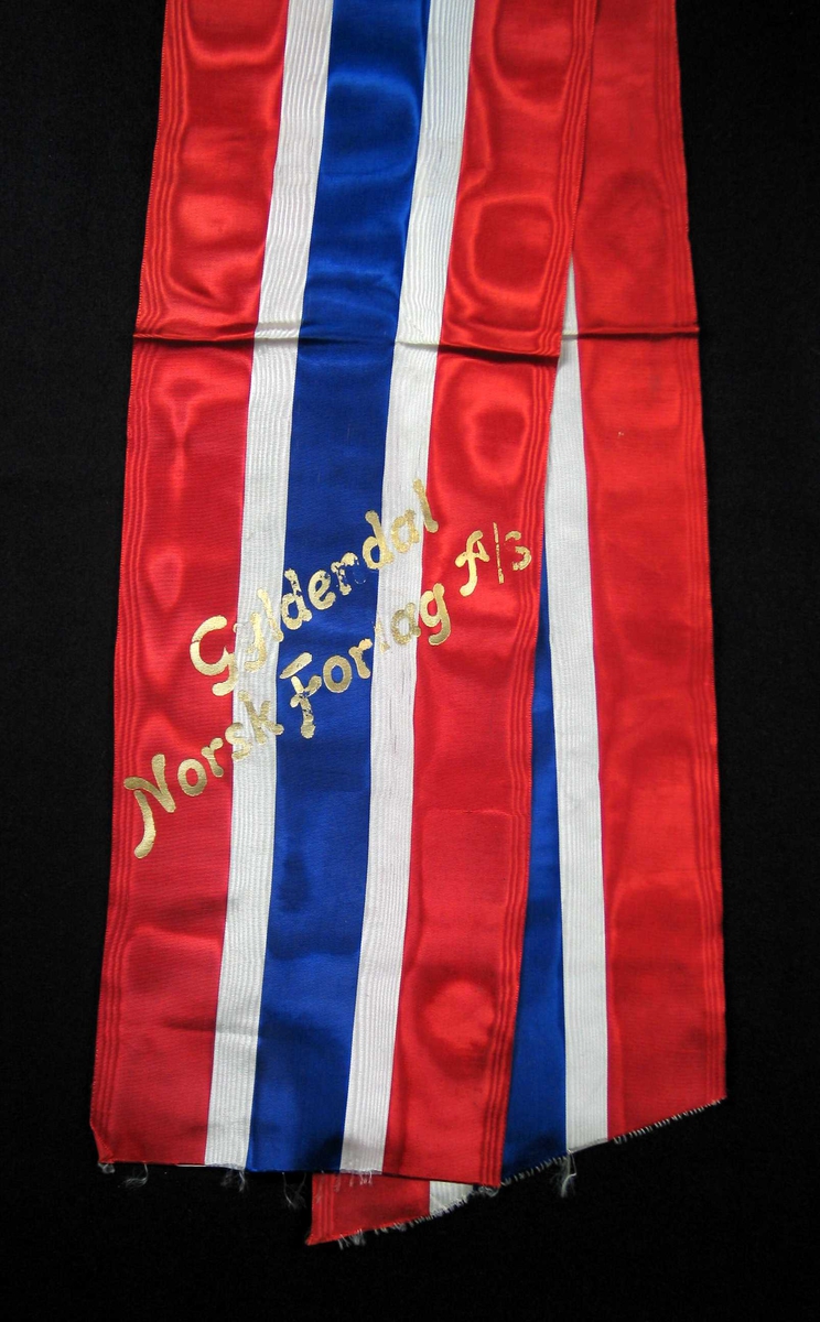Begravelsessløyfe i rød, hvit og blå silke med tekst i gull.