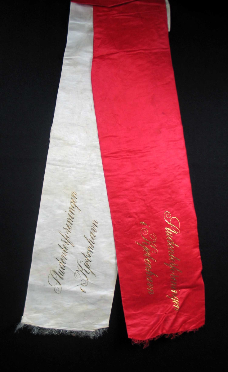 Begravelsessløyfe i hvit og rød silke med tekst i gull.