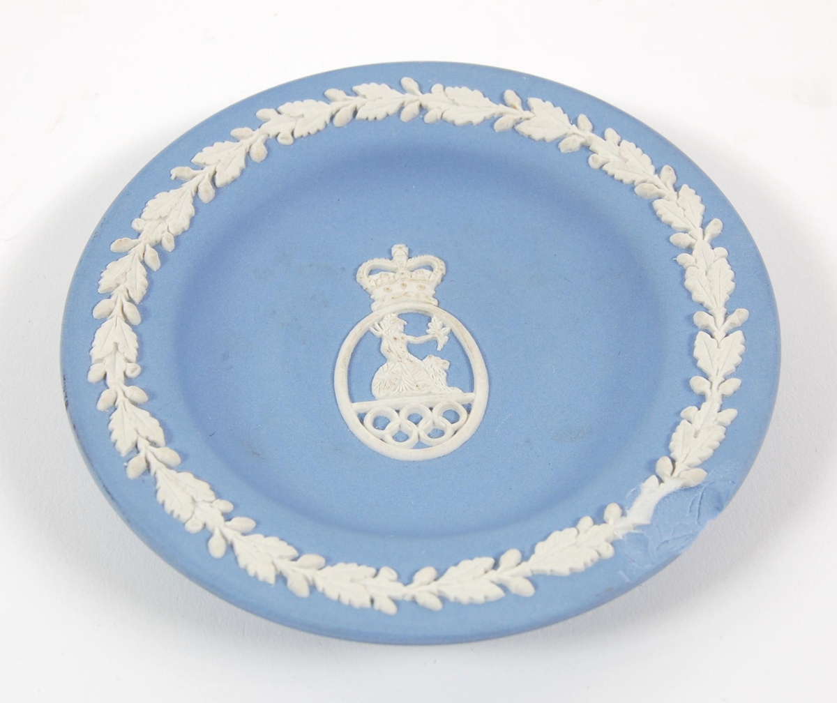 Blå skål med hvit dekor. Motivet på skålen er av en dame som sitter på en løve. De olympiske ringene inngår også i motivet. Det er et skår i skålen.
