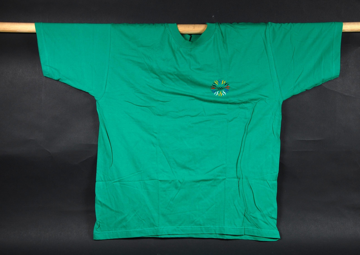 Grønn t-skjorte med to flerfargede logoer for "International Year Of Sport And The Olympic Ideal". T-skjorten er i størrelse XL.