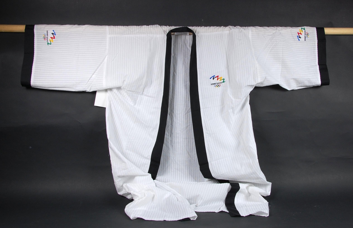 Hvit slåbrok med sort kantbånd og tre broderte logoer for de olympiske leker i Sydney i 2000.