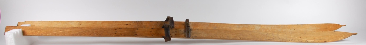 Ett par treski med bindinger. Bindingen består av en lærreim og en metalllås som strammes med en skrue. Skituppene har forlenget spiss.