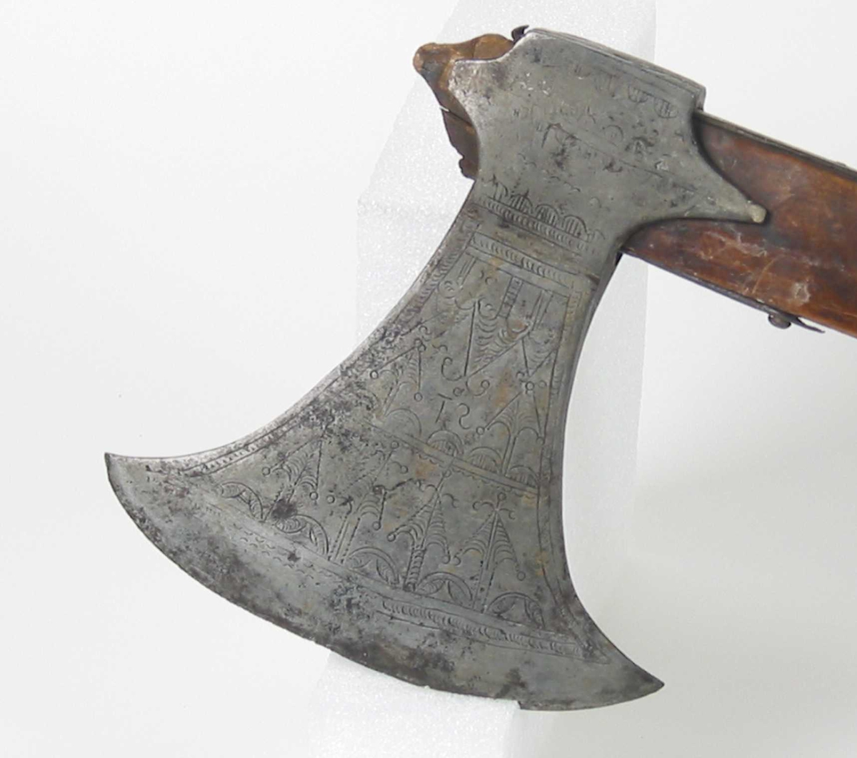 Symmetrisk blad. Bladet er tynt. 
Øsehammeren har skaftehull og fliker.
Etset dekor på begge sider. Stemplet TS på venstre side.
Gammelt treskaft med to orginale jernskinner med gravert dekor.
Jernskinnene er festet med nitter.
