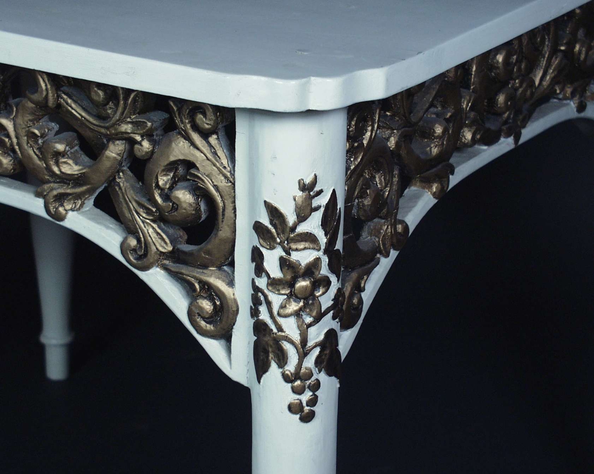 Hvitt bord i furu med akantus sarg.
Øverst på bena er det blomster utskjæringer.
Både akantus og blomserutskjæringene er malt med gull.