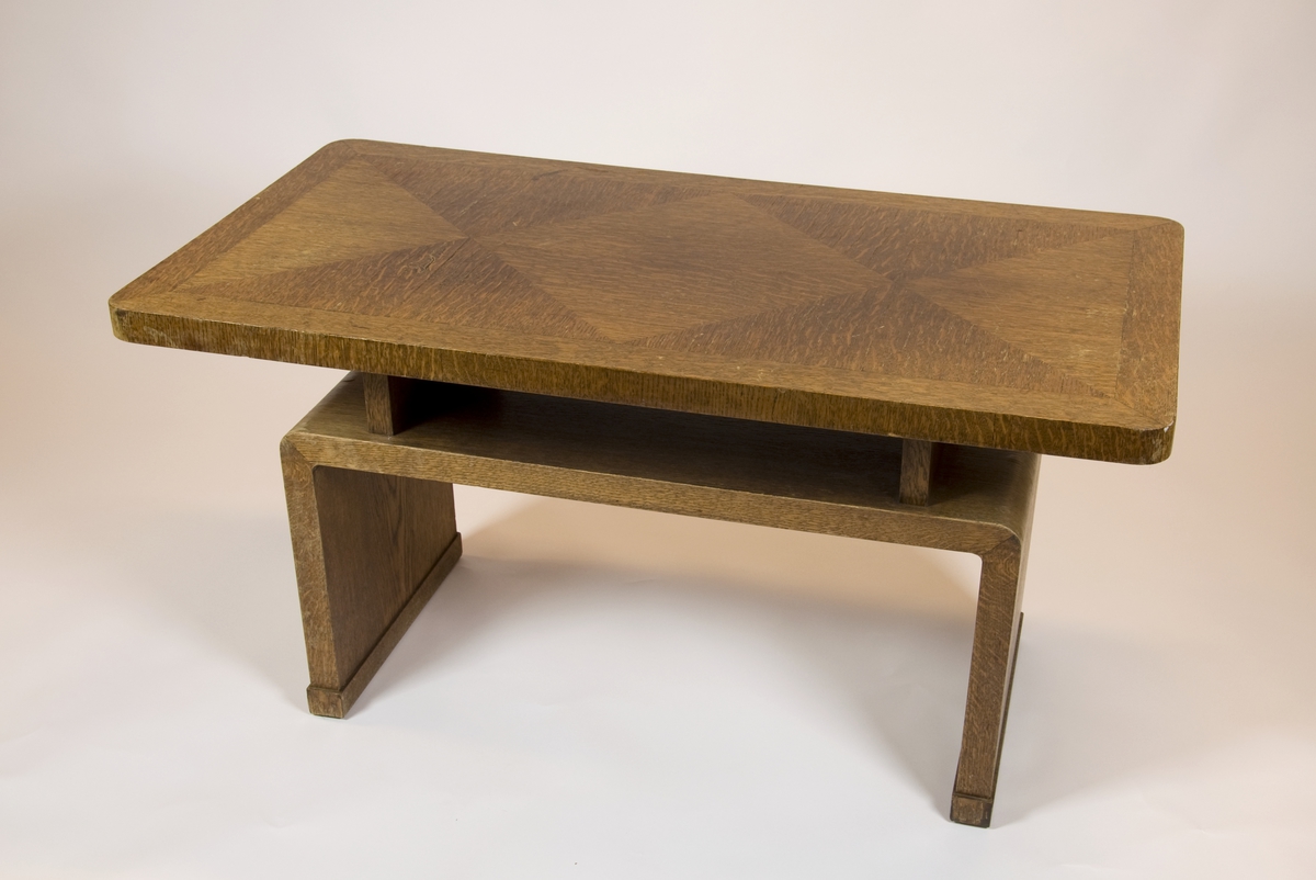 Salongbord av gran med eikefiner. Forholdsvis tykk bordplate, avrundet i hjørnene. Understellet er en bukk, en bøyd plate som danner en hylleunder bordet, der bordplaten hviler på to oppstående planker.