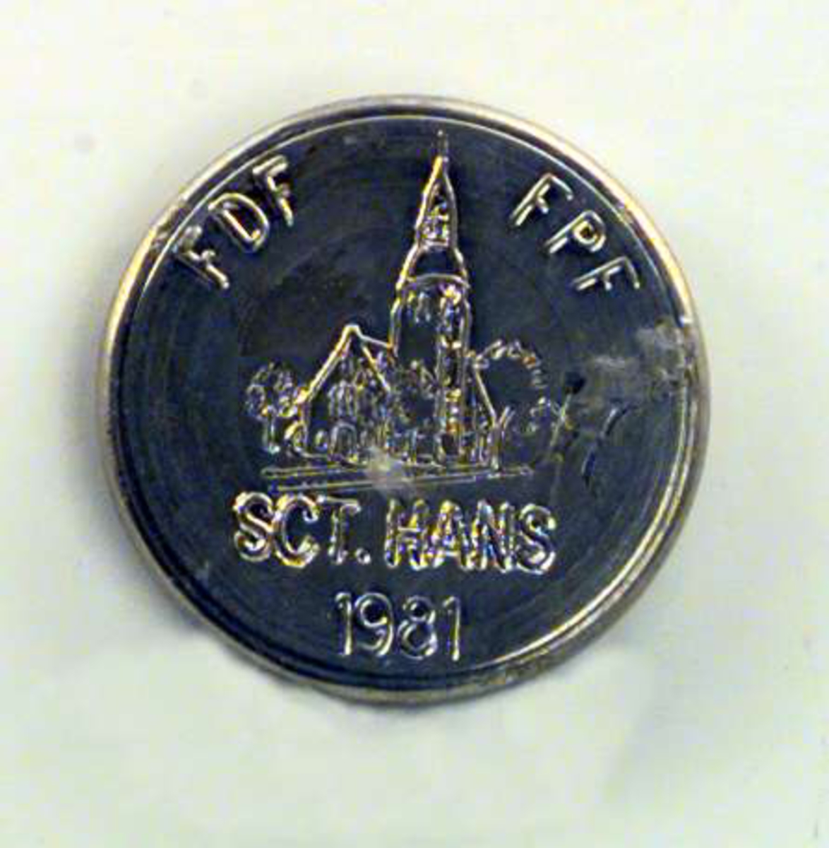 Medaljong i sølv. Motivet på medaljongen er en kirke og den har inskripsjonen SCT. HANS 1981.