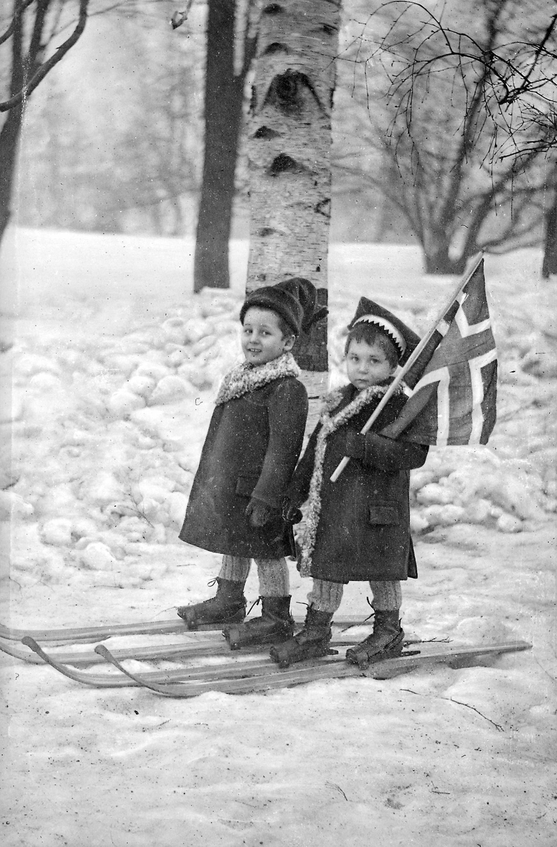 Portrett av to barn på ski med det norske flagget, vinter