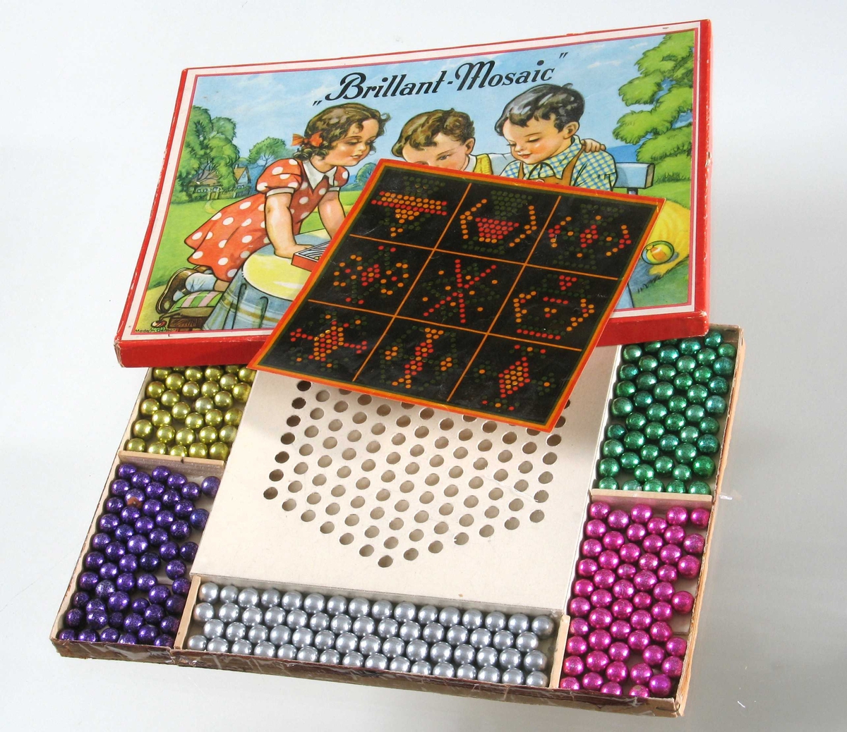 Motiv på esken: 2 gutter og 1 jente ved bord i en hage, leker med liknende spill. 