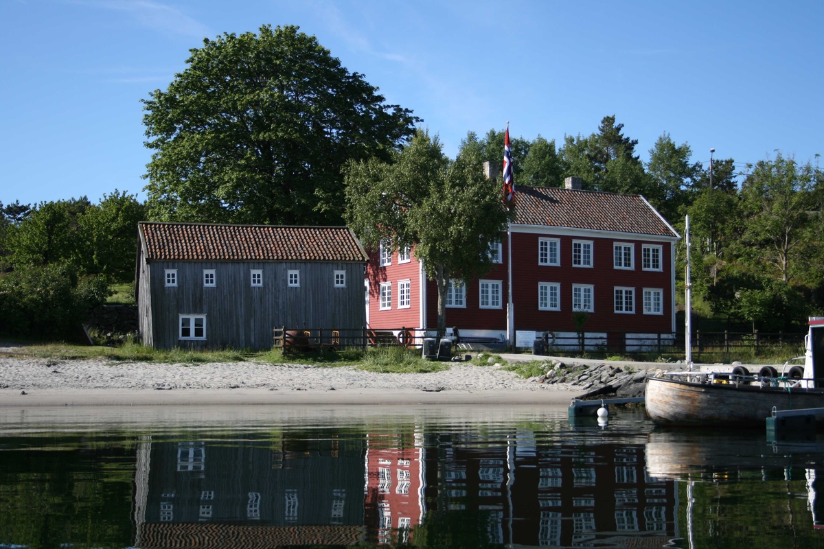 Merdøgaard, gårdstun sett fra N, sjøbod og våningshus. Tuntreet, en stor lønn, synlig over sjøboden.