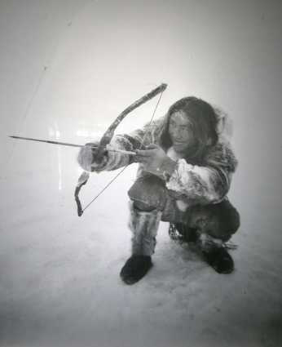 Fotografi på glassplate i dør, sort-hvitt. Viser eskimoen Ugpi med bue og pil.. Sign Worm-Petersen repro.