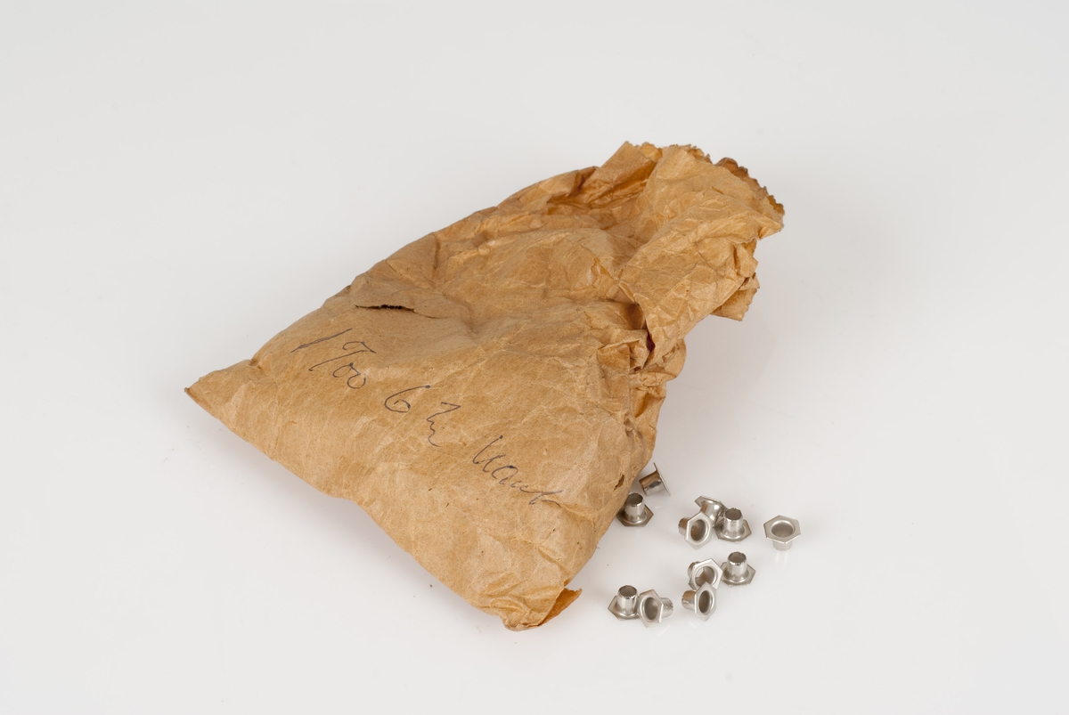 Maljer av metall i en papirpose som ligger i en plastpose.
Maljene er 6 kantet.