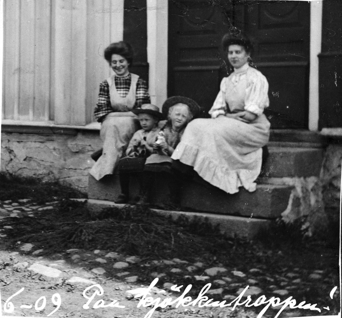 To piker og to voksne kvinner på en trapp, hushjelper
