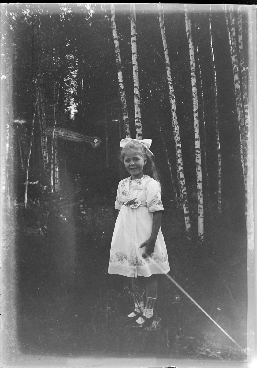 En jente i hvit kjole og sløyfe på hodet ute i skogen.