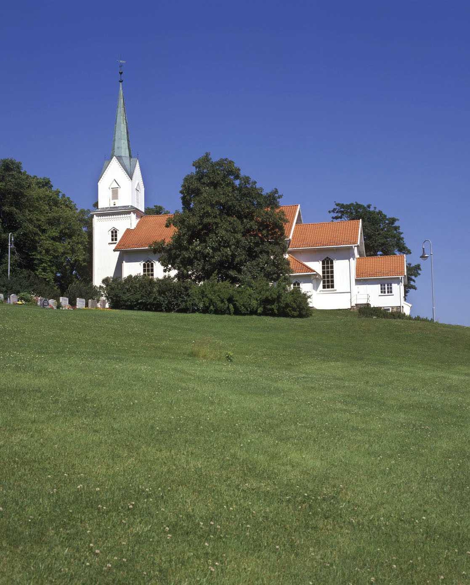 Rælingen kirke, lengderetning, gravplass i bildets høyre side, gressplen i forgrunnen. 