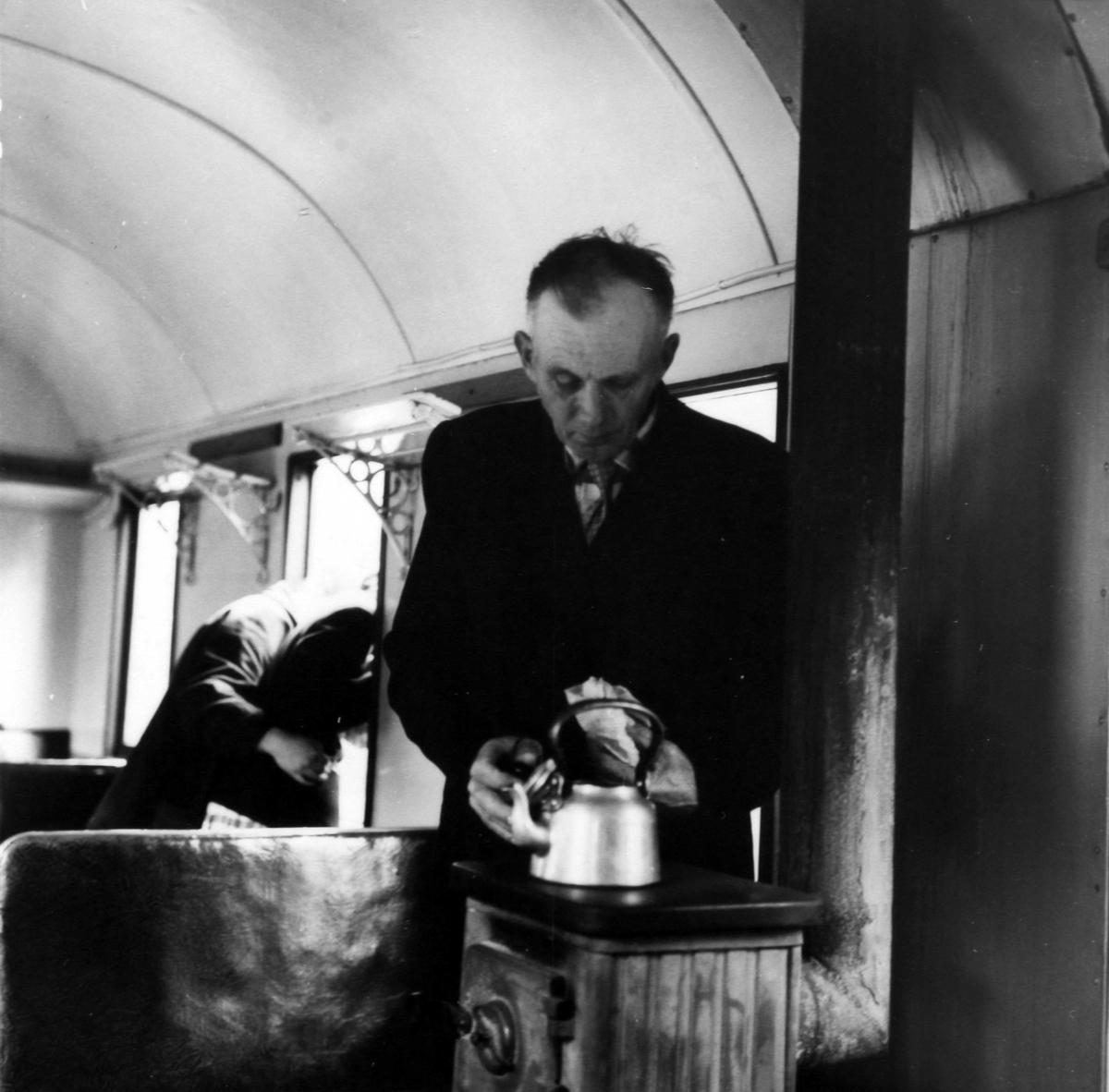Vogn BCo3 - interiør. Reisende (later som om han) koker kaffe på vedovnen.