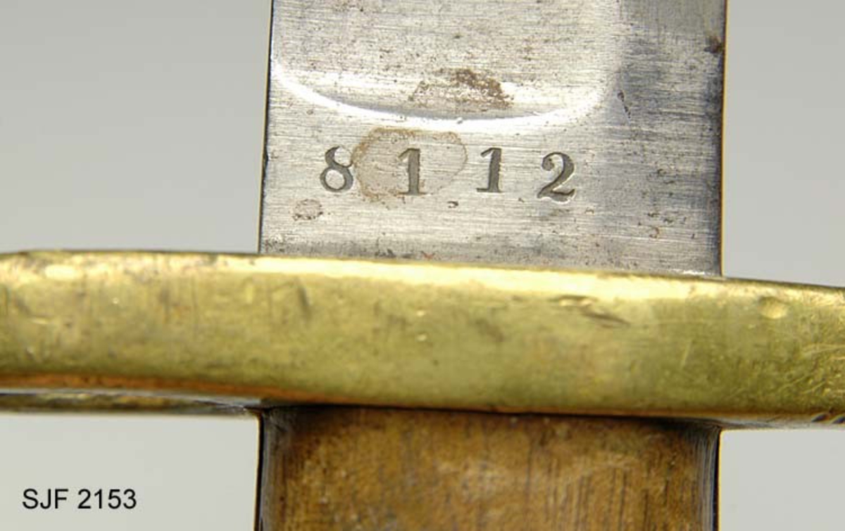 Sabelbajonett av type M/1860.  Våpenet har 57, 5 centimeter lang klinge, der den bakre delen er hulslipt i cirka 41 centimeters lengde på begge sider.  Her er klingen enegget.  Den fremre delen av sabelbajonetten er tveegget.  Bakerst på klingen oppunder parérplata, er det to K-er med kroner over (Kongsberg våpenfabrikks symbol) på den ene sida, og ei sifferrekke (8112) på den andre.  Grepet består av to treplater som er klinket mot tangen, mellom parérplata (foran) og et messingbeslag (bak) med spor for bajonettklakken (festing).  På den ene sida sitter det en fjærbelastet knapp som står i forbindelse med utløserklakken. Parérplata har et sirkelrundt hull med diameter på 1, 9 centimeter, som skulle tres inn på geværpipa.  I enden av det nevnte endebeslaget på grepet er det et gjennombrutt hull med en lærstropp. 

Sabelbajonetter av denne typen ble brukt til firelinjers kort kammerladingsgevær (M/1860).  Denne bajonettypen er en variant av M/1859, som ble konstruert for 15-lødig tappstusser, 18-lødig kammerladingsgevær og avkortete kammerladingsgevær.  Diametrene på slike våpen var noe større enn på kammerladingsgevær M/1860, og dimensjoneringa av parérplatene ble følgelig noe ulike på de to nevnte utgavene av sabelbajonetten fra Kongsberg våpenfabrikk. Dette var for øvrig de første bajonettypene som kunne festes under geværpipa, noe som ble mulig da det kom geværtyper som ikke hadde ladestokk.  På eldre militære geværer ble bajonettene plassert på den ene side av geværpipa, noe som skal ha medført at skuddene hadde en tendens til å trekkes noe sidevegs i forhold til de målene skytterne siktet mot.  Denne bajonettypen ble tilgjengelig omkring 1860, i første omgang for infanteriavdelingene, etter hvert også for artillerister.  I tillegg til de to nevnte sabelbajonettene ble det også produsert en noe mindre variant av denne sabelbajonetten til bruk på Krigsskolens kammerladingsgeværer. 

Bajonetten har tilhørt Kolbein Helstad, Gjesåsen. 
