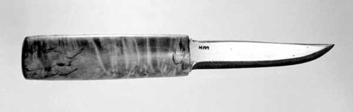 Kniven er en brukskniv med skaft av valbjørk. Bladet svinger svakt oppover mot odden. Den er stukket inn i en knivkjuke (SJF 3215). 
Kniven er ubrukt. 
