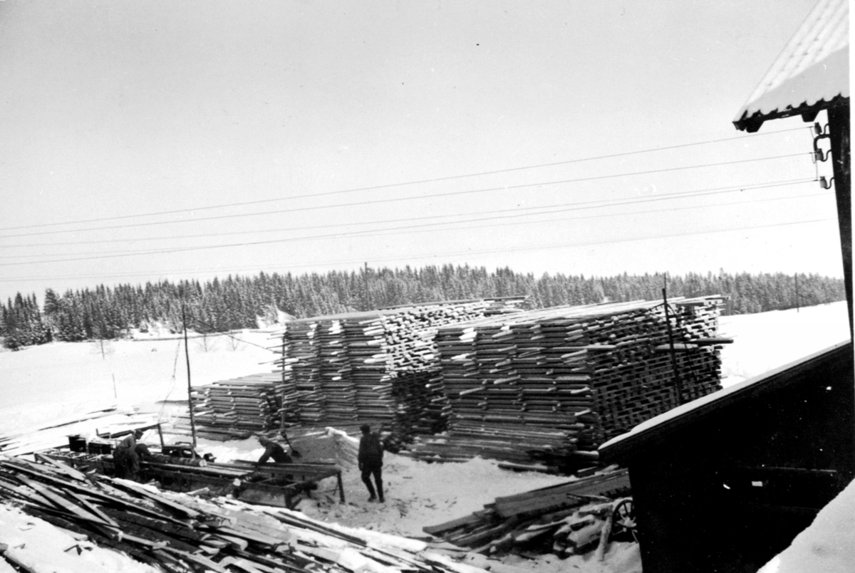 Skjæring av tømmer til materialer. Planker lagt opp for tørking. Sagbruk på Lodviken, Helgøya. 3 menn jobber.
