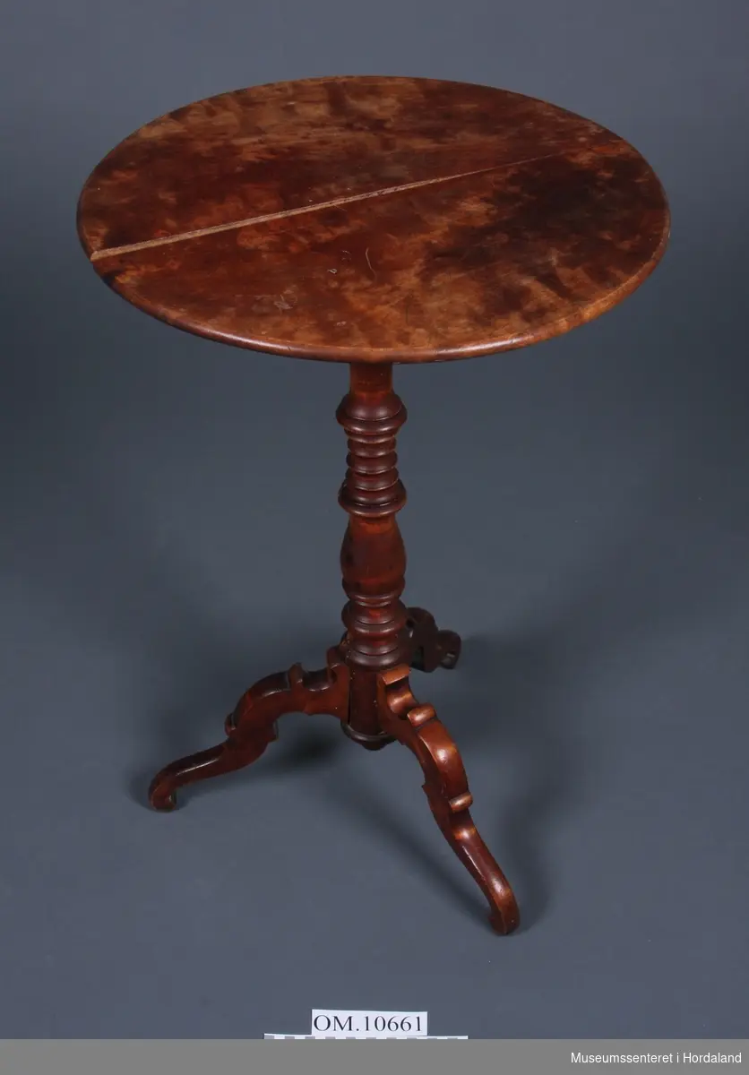 Form: Lite rundt, høgt bord med tre bein nedst på høg stamme. Stammen er dreid.Bordplata er delt i to og er ikkje heilt saman.