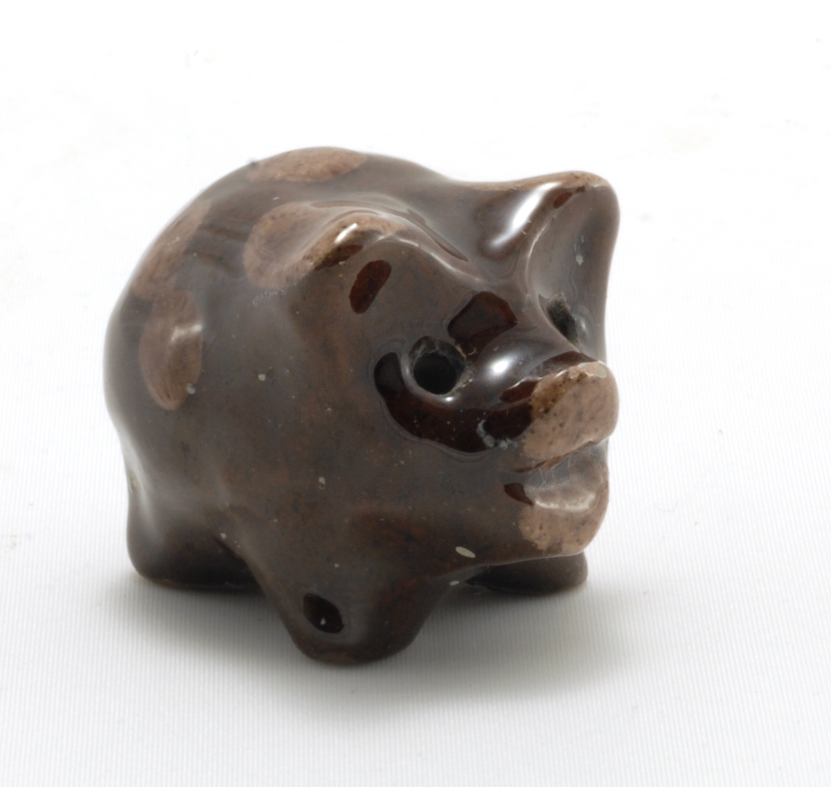 Liten gris med glasur. Modellert med 4 bein, nese og ører. Ører og nese samt felter malt i lysere brunfarge.