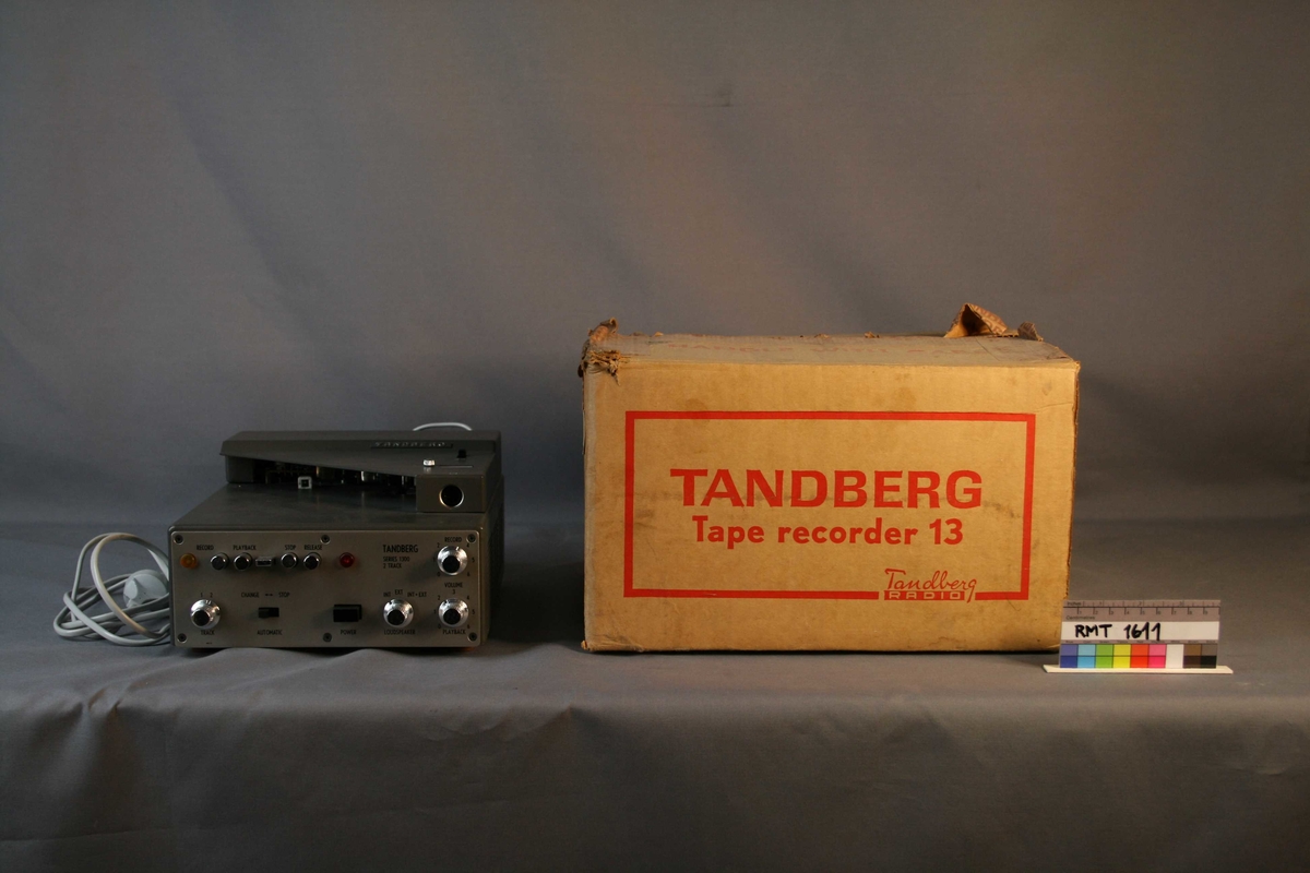 Brun rektangulær pappkasse. Tape med Tandbergs logo er festet til kassen. Isopor inne i kassen, for beskyttelse og stabilisering av båndopptakeren.