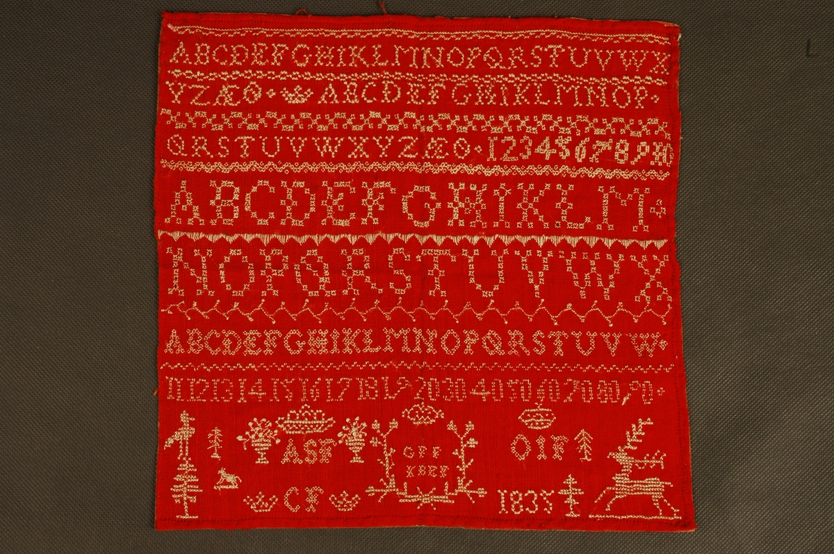 Navneduk fra 1835 med alfabetet påbrodert, tallene 1 til 9, blomstermotiv, dyremotiv og ulike border. Duken  har påsatt papir på baksida.