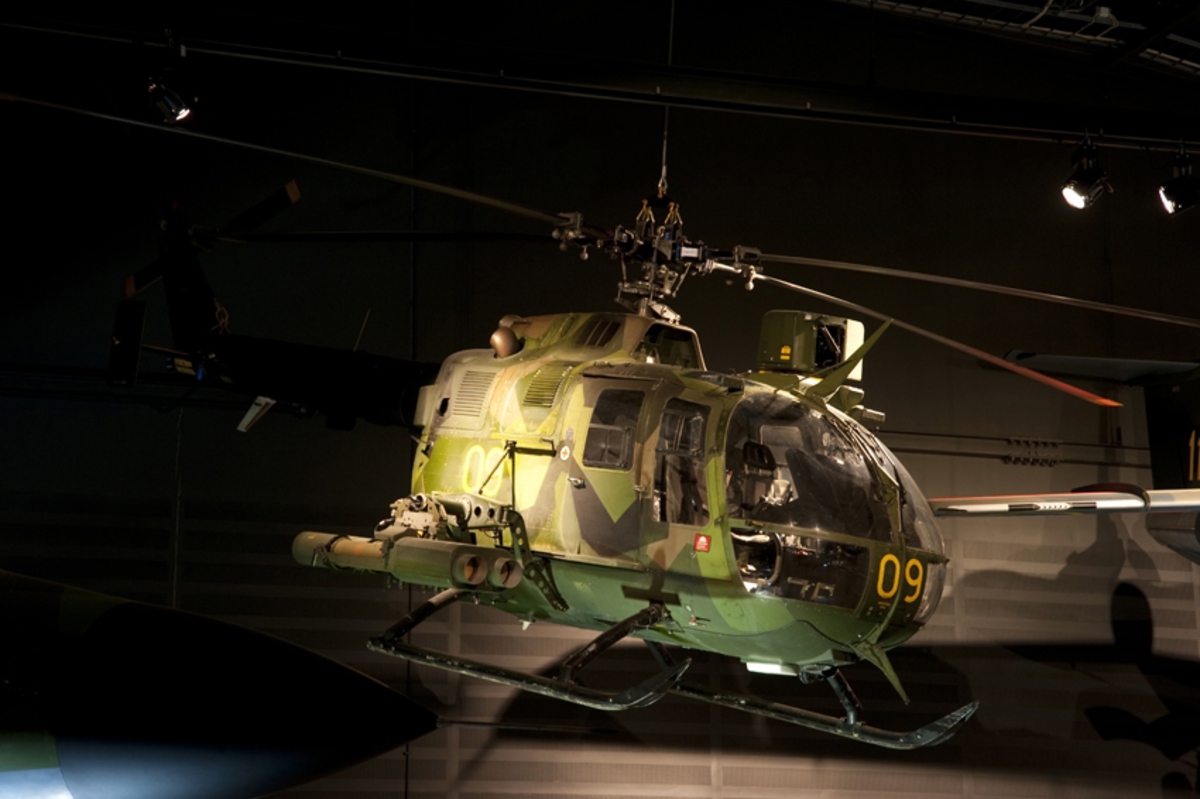 Helikopter, Hkp 9A. 
MBB BO 105 CB3

Kamouflagemålad attackhelikopter, utrustad med två turbinmotorer. Längst med sidorna sitter medar. Beväpnad med fyra robotkapslar. Tvåsitsig. Ovanför huv sitter siktesinstallation. Fyrbladig rotorinstallation på ovansidan samt mindre tvåbladig rotor på fena.
Märkning: Kodsiffra 09 fram och på sidan, kronmärke på bakkroppen samt bak sitter texten Försvarsmakten.