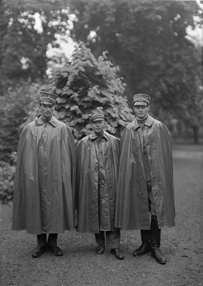 Porträtt. Tre löjtnanter iförda regnrock i en parkmiljö på Malmen.