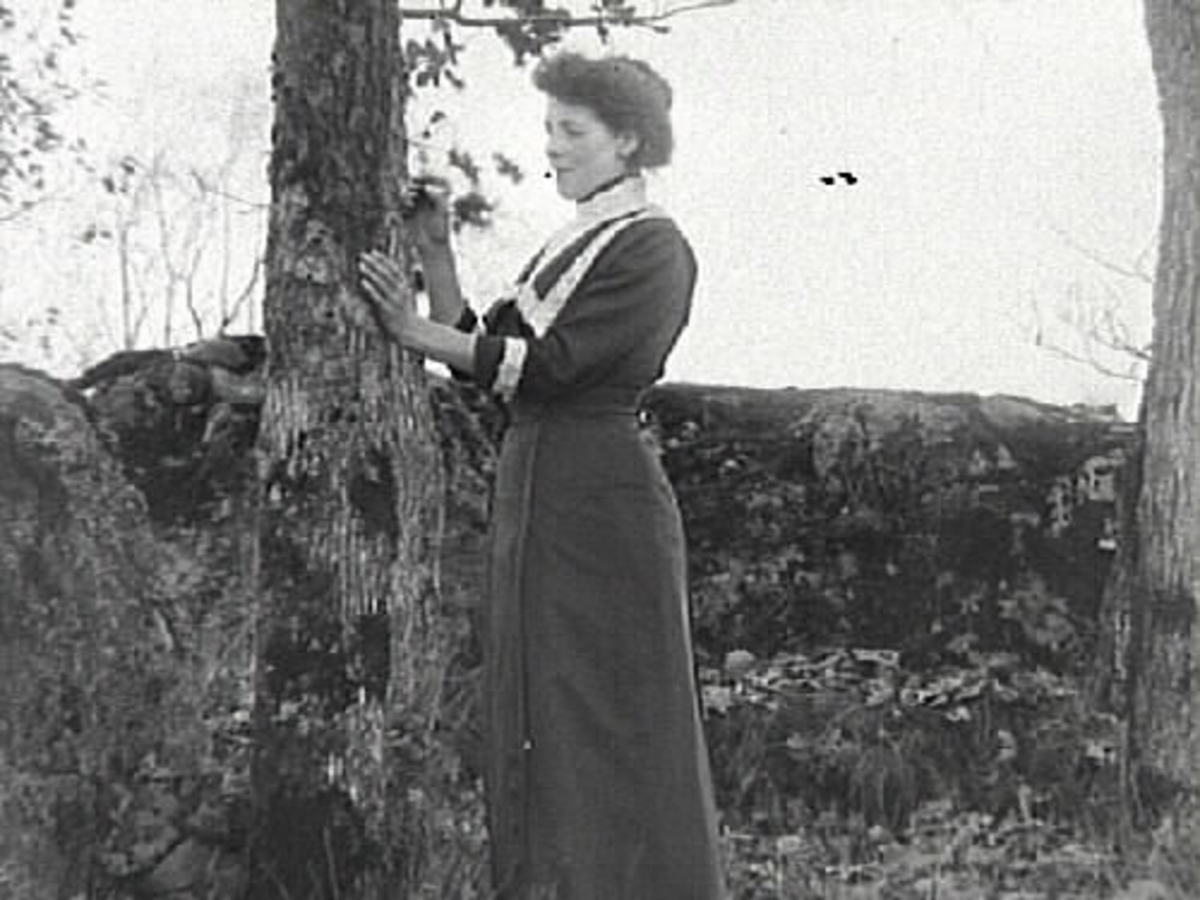 Kvinnoporträtt. En kvinna fotograferad utomhus stående vid ett träd.