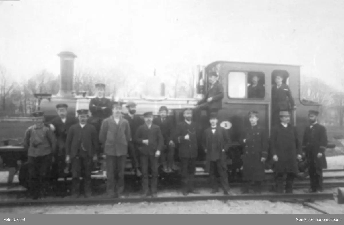 Gruppebilde av 16 jernbanefolk foran Setesdalsbanens damplokomotiv type XXI nr. 1