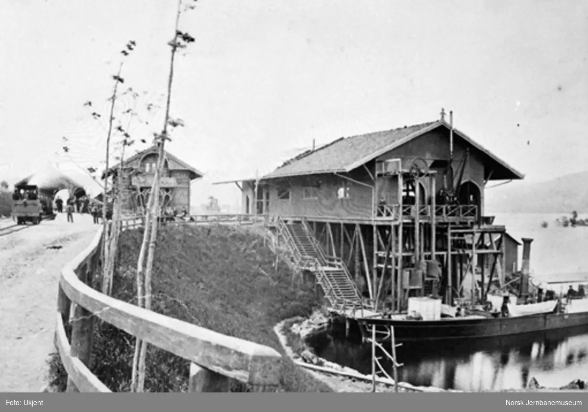 Dampbåten "Harald Haarfager" ved bryggen på Randsfjord stasjon, med stasjonen i bakgrunnen; damplokomotiv i spor 1