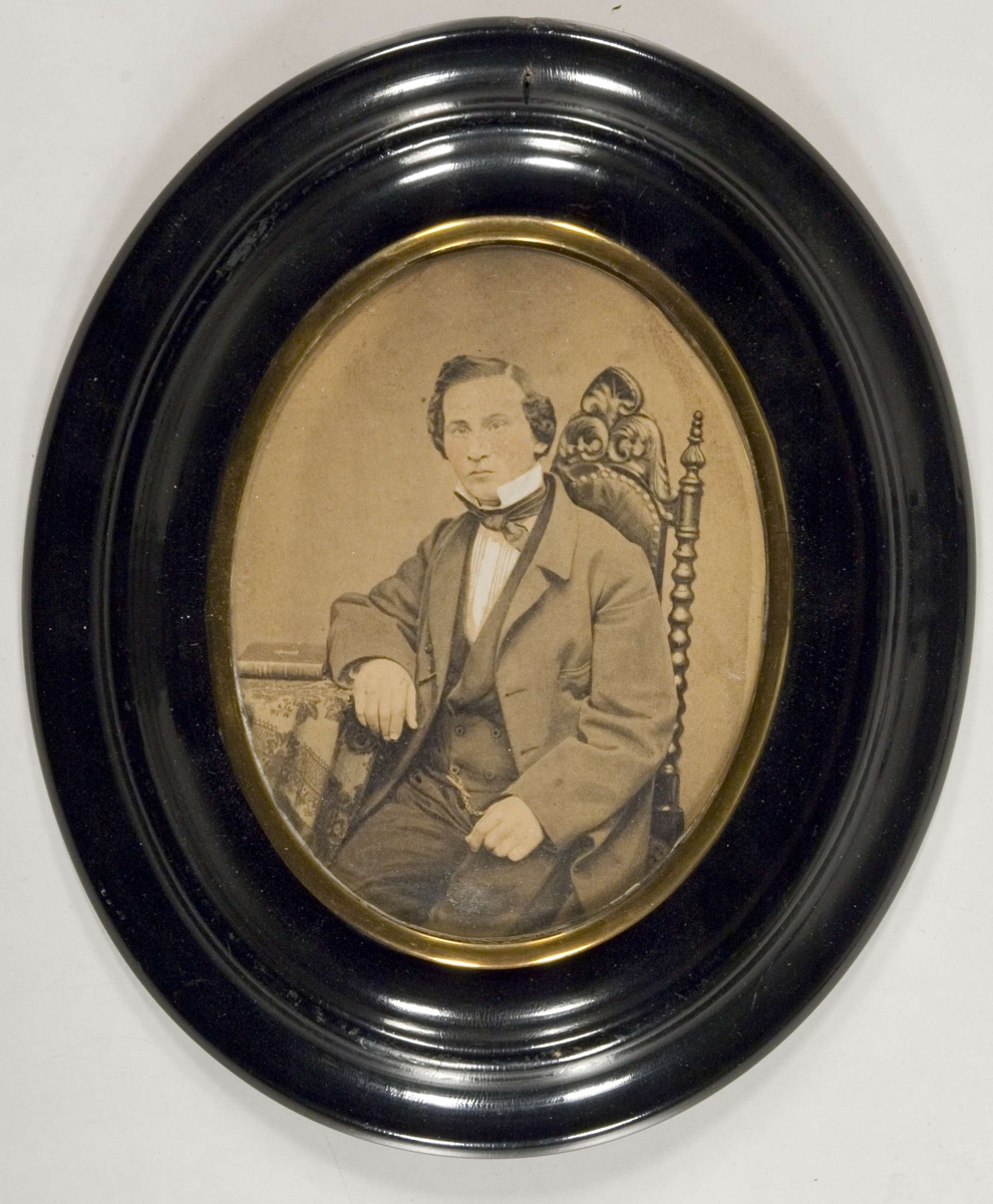 Portrett, mann sittende på høyrygget stol.