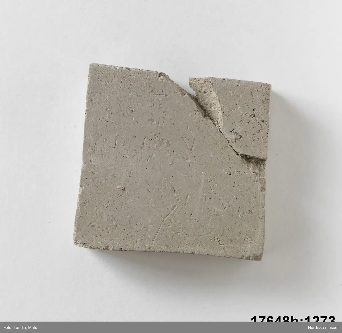 Rektangulär platta av bränd oglaserad grå lera. På en sida text: "Kakelugnsler".

Anm. ett hörn avslaget och påklistrat igen.
/Leif Wallin 2014-01-07